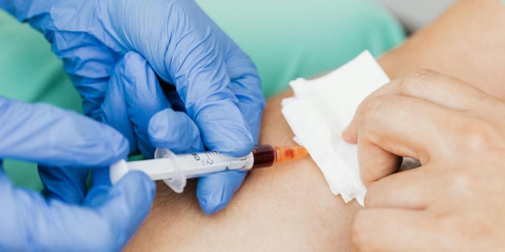 handen van zorgkundige met handschoenen nemen bloedstaal bij iemand af 