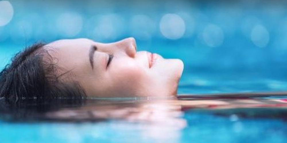 vrouw drijft op de rug met ogen toe in stil water 