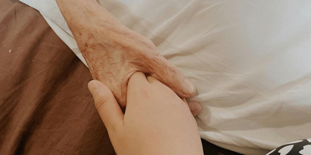 hand van volwassenen houdt hand van oudere zorgbehoevende vast