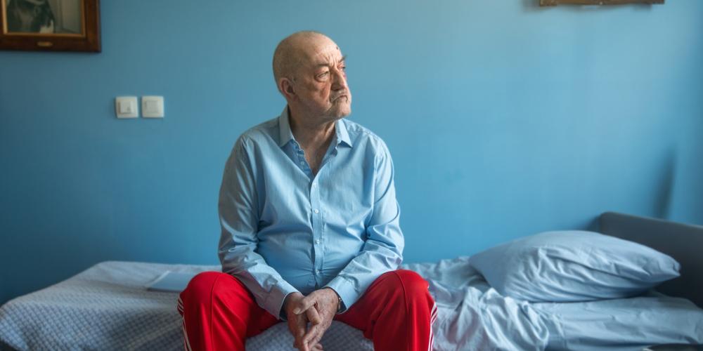 Personage Horst zit op bed starend door raam 