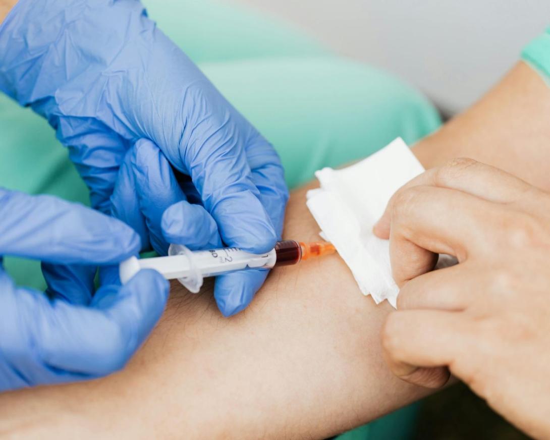 handen van zorgkundige met handschoenen nemen bloedstaal bij iemand af 