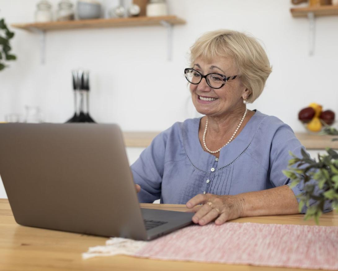 Vriendelijke oudere dame volgt webinar met laptop in de keuken